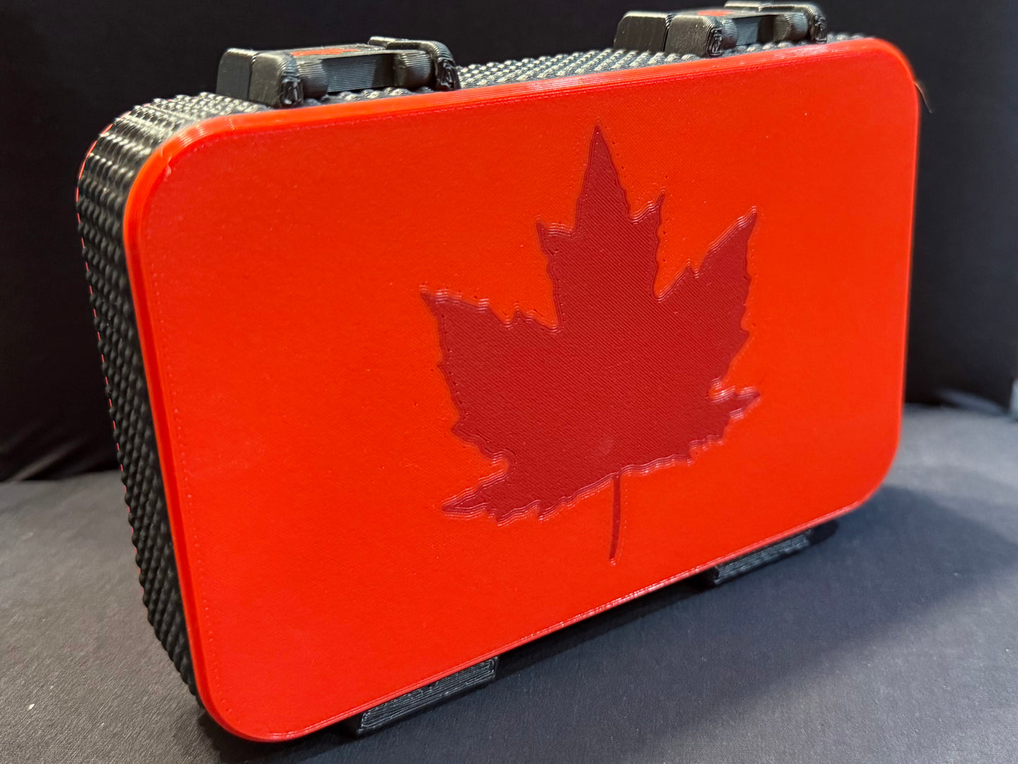 Front view of Canadian-made harmonica case in light-red, black, with a dark-red embossed maple leaf design.