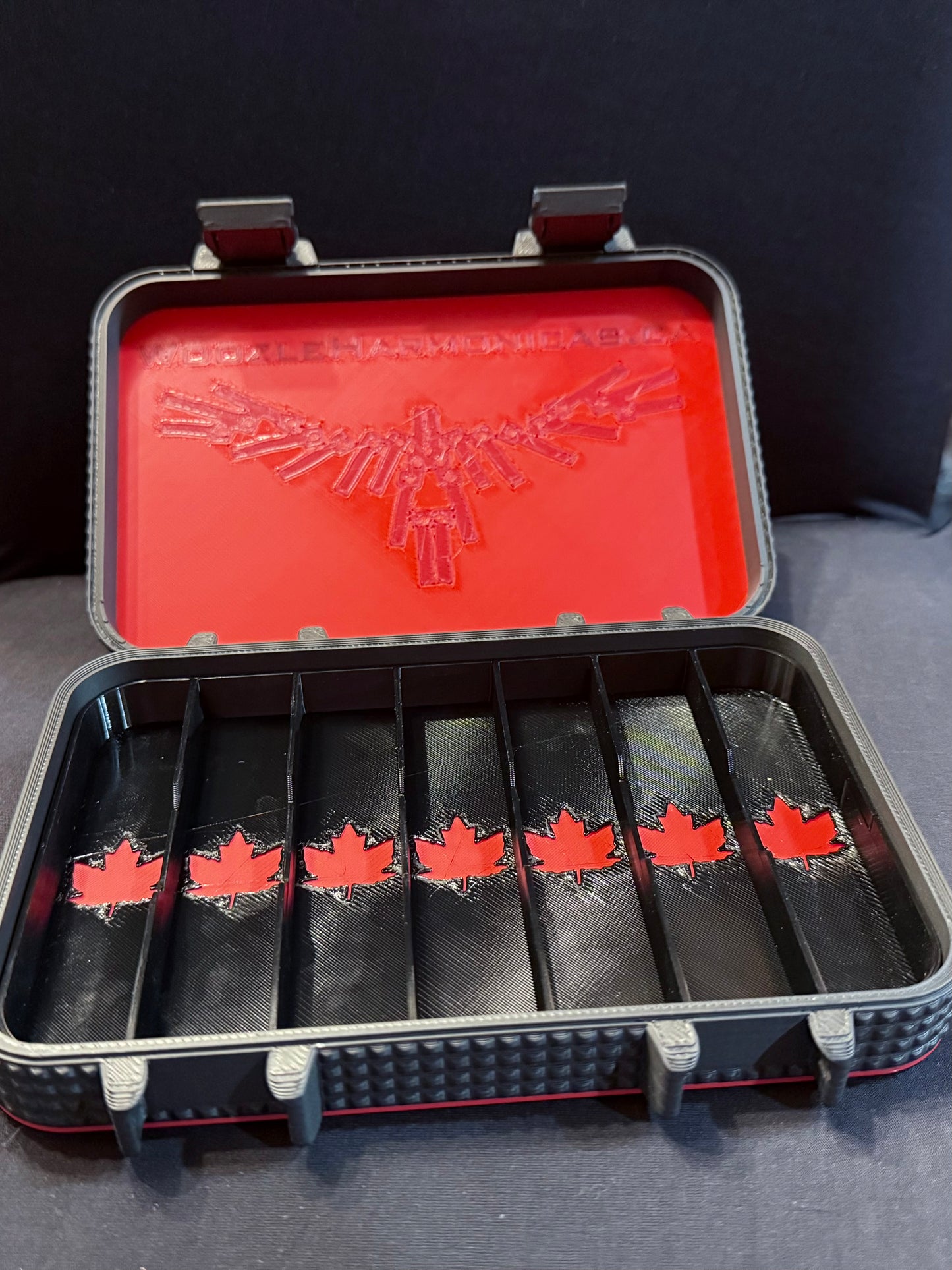 Interior view of empty 7-slot harmonica case with red maple leaf dividers and Woozle Harmonica emblem inside the lid.