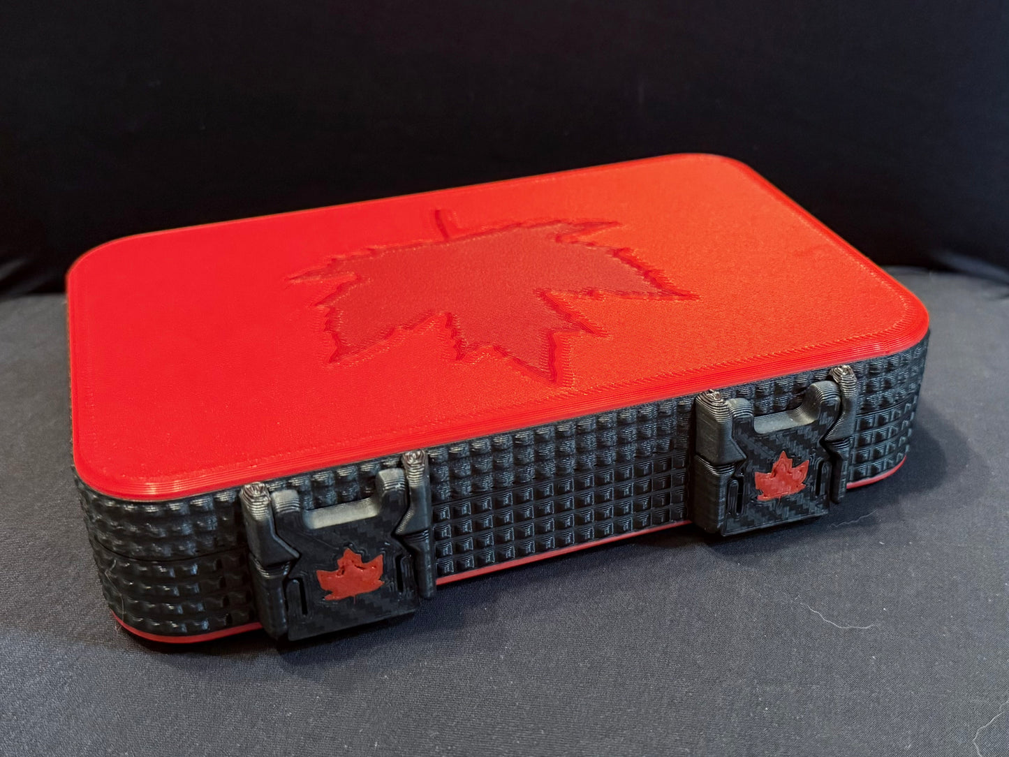 Side angle of harmonica case highlighting carbon-textured black sides and maple leaf latches.