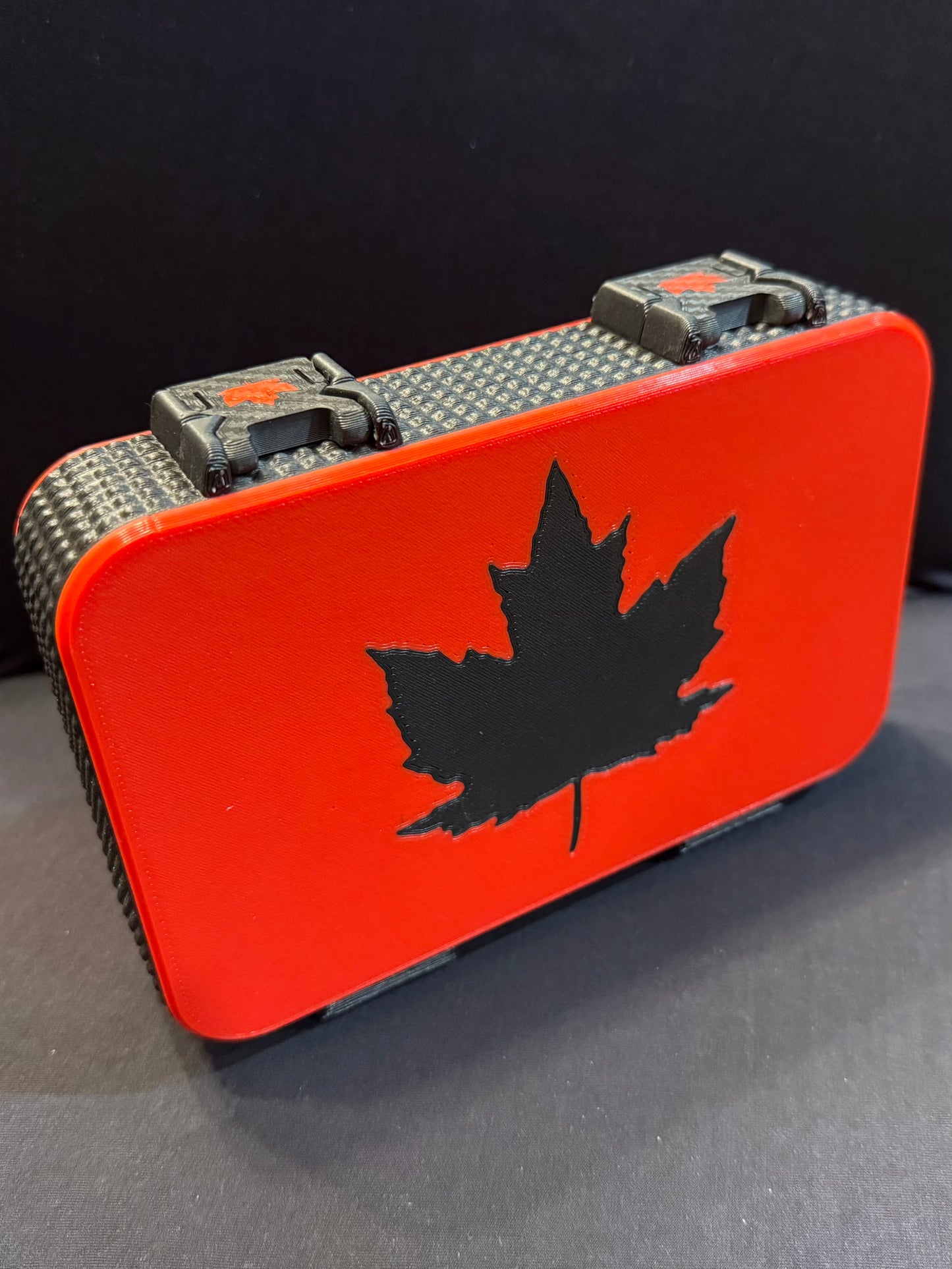 Harmonica case with matte black maple leaf inlay against a rich red top, black textured sides, and dual latches.